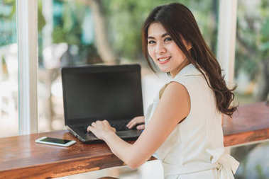 亞洲女人微笑與同時使用筆記本電腦