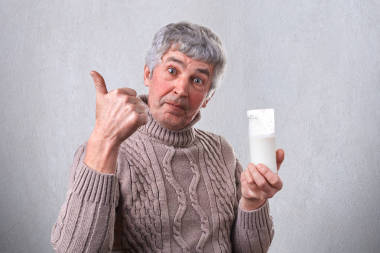 高級的英俊的男人有令人愉快的外觀顯示與他的拇指他手里拿著一杯牛奶，他喜歡它。男人廣告可口的牛奶。正在高興地喝牛奶的人