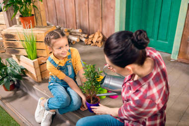 高角度觀母親與微笑著女兒坐在門廊上，給植物澆水