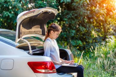 年轻的亚裔女子，坐在笔记本，向客户发送工作的自由职业者使用笔记本的掀背车