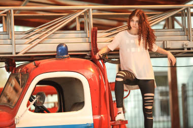 復(fù)古消防車和漂亮的少年。年輕漂亮的女孩白色與紅色卷曲的頭發(fā)和黑色破舊的牛仔褲，構(gòu)成附近老消防車的室外肖像