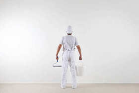 后视图的画家男人看着空白的墙上，用油漆罗尔