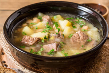 土豆、 豆类和韭葱石背景上的陶瓷碗里的牛肉汤