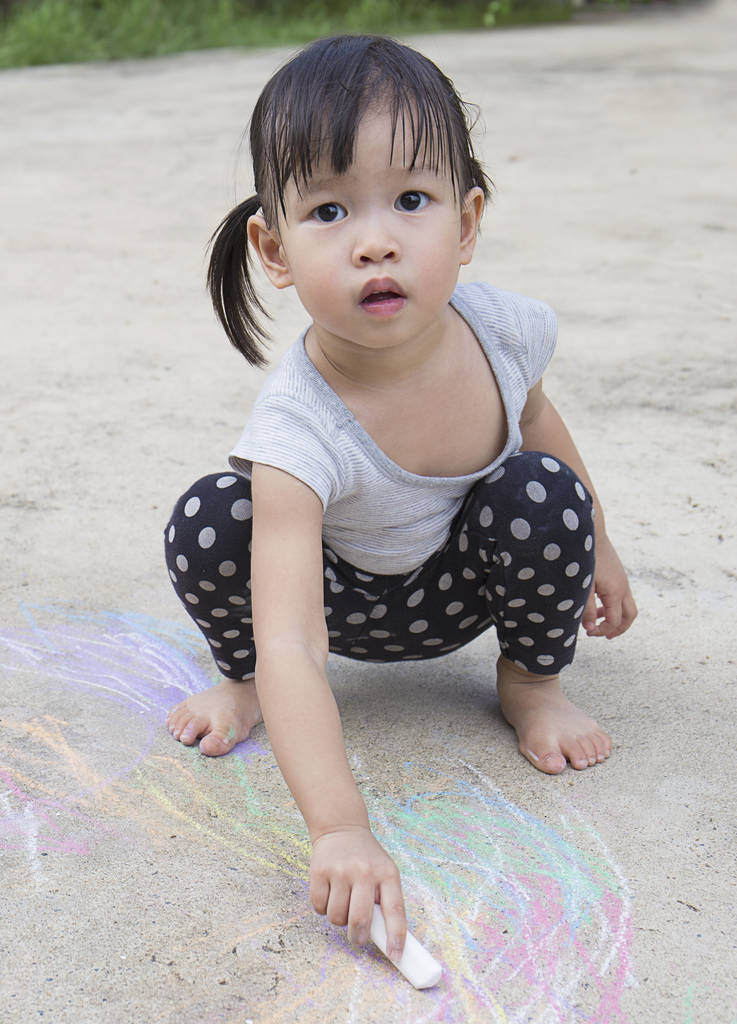 小亚洲女孩在沥青户外画与粉笔