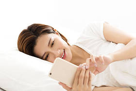 年轻女子看着躺在床上的智能手机