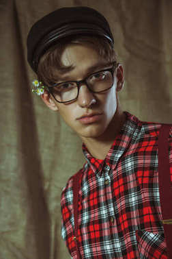 一个年轻的家伙，在一顶黑帽子、 眼镜和耳朵后面的花