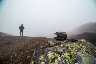 霧在山中的人。徒步旅行者爬上巖石上面有霧谷峰。在前臺(tái)路標(biāo)喜歡從石頭金字塔