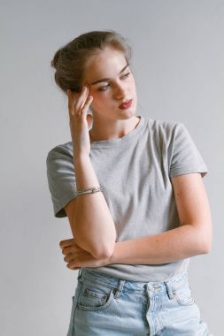 美麗，可愛的姑娘，穿著牛仔褲和一件運動衫站附近白墻