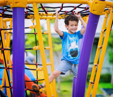 一個(gè)小男孩爬在幼兒園操場(chǎng)上繩