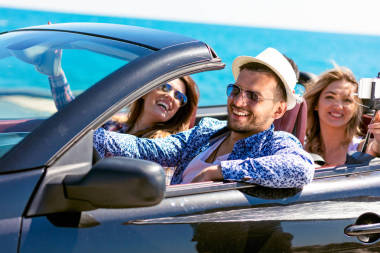 群快樂年輕朋友在敞蓬車與舉的手，駕駛著日落