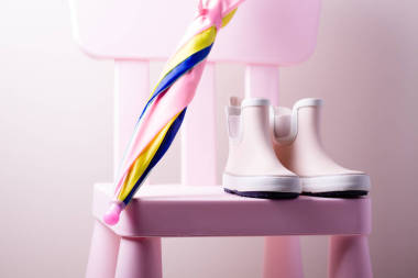 粉红色的小儿童橡胶靴与五颜六色的雨伞