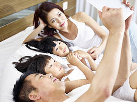 亚洲家庭有两个孩子在床上使用数字平板电脑
