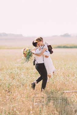 新郎的可愛的肖像在田野的背景下用五顏六色的花束紡著復古的新娘