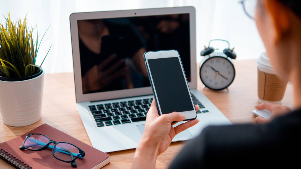 使用智能手机和笔记本电脑背景的女性手是工作场所表