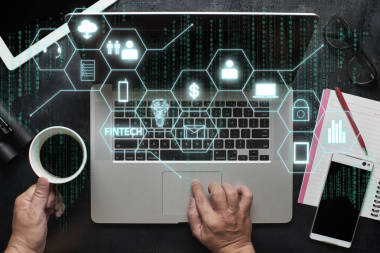 “Fintech”字在數(shù)字虛擬屏幕上以筆記本電腦、男手、筆記本、眼鏡、寫生本、黑色木桌為背景。高科技的經(jīng)營理念