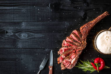燒烤干歲的肋的牛肉、 香料、 蔬菜以及一杯淡啤酒特寫黑色木制背景
