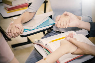 年輕人坐在圈子里, 手牽著手, 在教室里祈禱考試