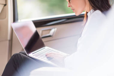 在汽车中使用的笔记本电脑的女人