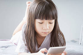 小亚洲女孩使用智能手机和躺在床上。儿童上瘾手机