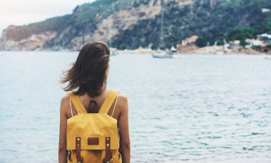 備份視圖時(shí)髦女孩與砂海岸線在背包上自然景觀模擬。對(duì)背景的海灘海景和地平線山的旅行者。旅游看在藍(lán)太陽的海洋，夏季放松的生活方式