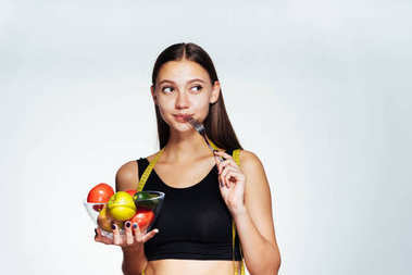 一個(gè)的年輕的女運(yùn)動(dòng)想要減肥，在她手里捧著一盤有用的蔬菜和水果