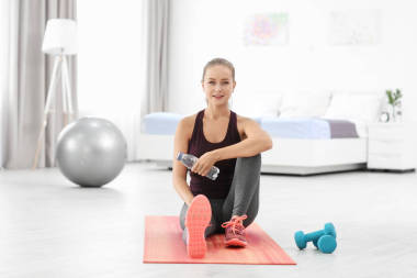 年輕運(yùn)動(dòng)的婦女與瓶水坐在席子在家