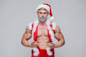 圣诞节。性感的圣诞老人。年轻的肌肉男穿圣诞老人帽子展示他的肌肉