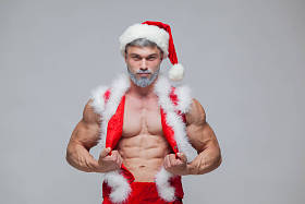 圣诞节。性感的圣诞老人。年轻的肌肉男穿圣诞老人帽子展示他的肌肉