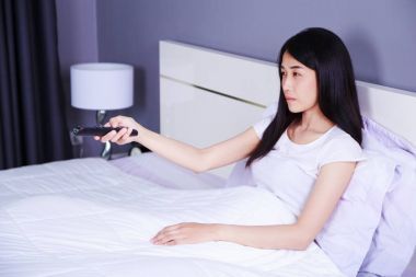 臥室的床上有遙控的婦女看電視