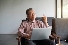 在现代轻型室内使用手提电脑的亚洲老人