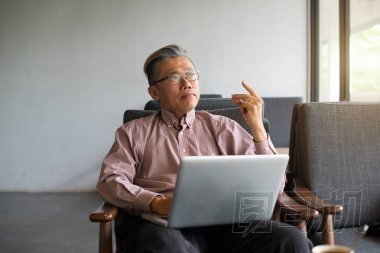 在現(xiàn)代輕型室內(nèi)使用手提電腦的亞洲老人