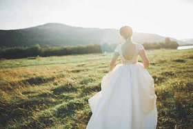 新娘穿着婚纱，与美丽的风景背景的草地上摆姿势