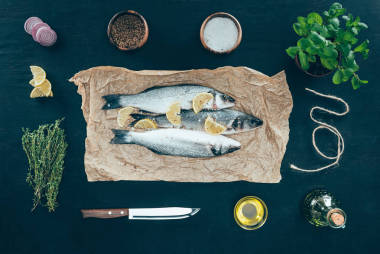烤紙上的檸檬片和黑色香料的美味魚的頂部視圖