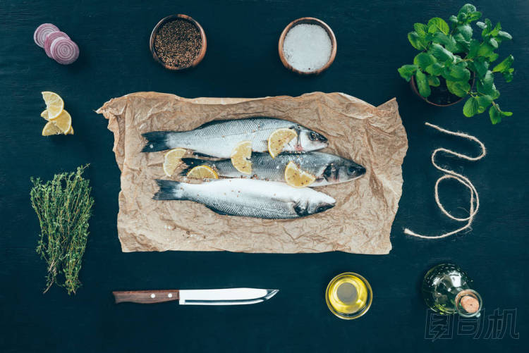 烤紙上的檸檬片和黑色香料的美味魚的頂部視圖