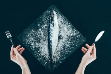 石板板上新鮮生鯖魚的頂部和人的手用叉子和刀子隔絕在黑色