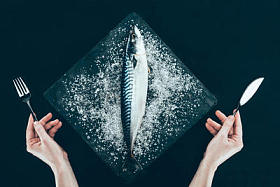 石板板上新鲜生鲭鱼的顶部和人的手用叉子和刀子隔绝在黑色