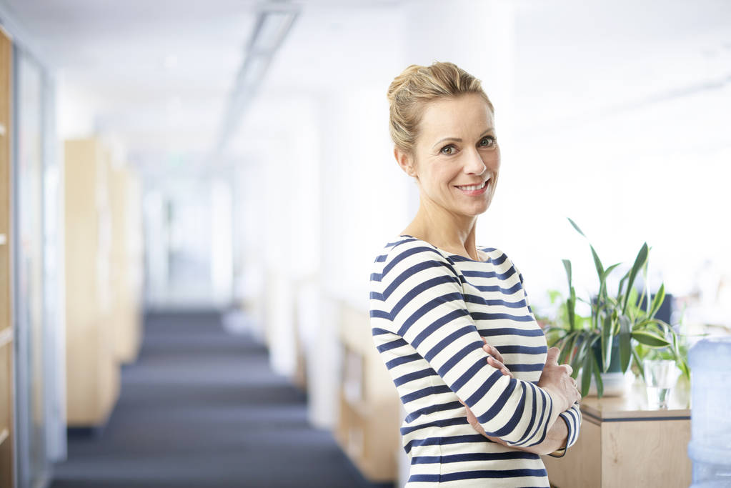 美丽的微笑成熟的女商人穿着便服双臂交叉站在办公室 美丽的微笑成熟的女商人穿着便服双臂交叉站在办公室