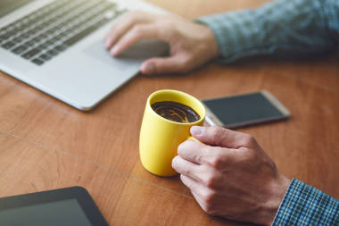 人喝杯子早晨咖啡在桌与膝上型电脑