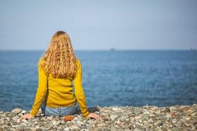 美丽的金发女郎坐在沙滩上, 看