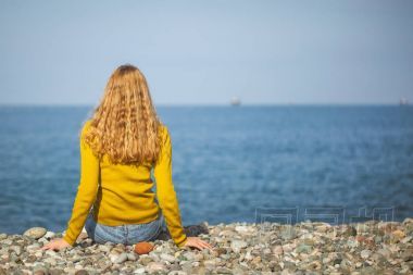 美麗的金發(fā)女郎坐在沙灘上, 看