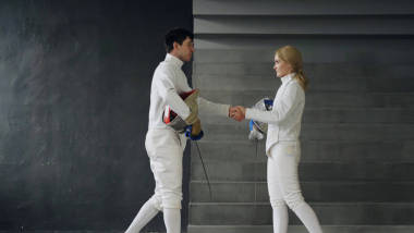 兩個(gè)擊劍男女在室內(nèi)擊劍比賽結(jié)束時(shí)互相握手