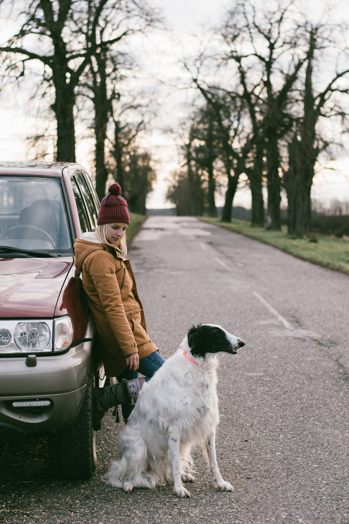 带着狗一个女人带着她的狗旅行在路上等待越野车