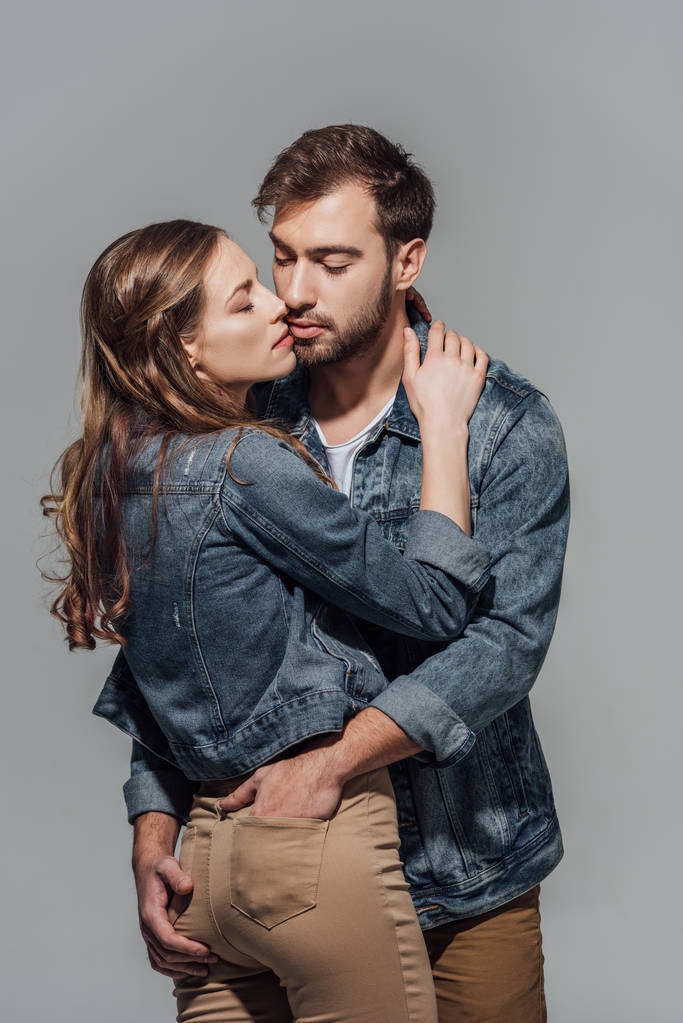 诱人的年轻夫妇在牛仔夹克拥抱孤立灰色 诱人的年轻夫妇在牛仔夹克拥抱孤立灰色