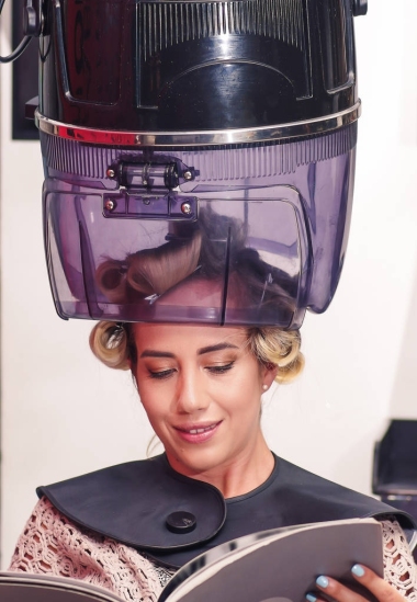 在一個模糊的背景下, 看著一本書, 在一個老的吹風(fēng)機椅罩下等待微笑的金發(fā)女郎關(guān)閉