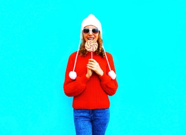 肖像俏麗的微笑的婦女咬住棒糖紅色針織 sw