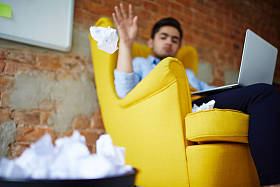 年轻人用手提电脑把纸球扔进垃圾桶