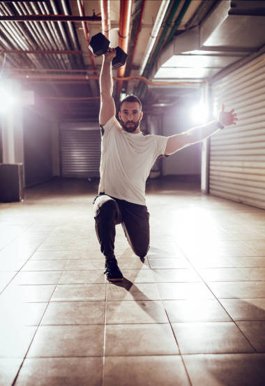 年輕的肌肉男子做頭頂弓步演習(xí)與啞鈴的交叉配合訓(xùn)練在車庫