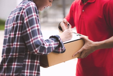 年輕的后勤職業(yè)概念。快樂送貨的人把他的包給客戶在家里。在真正的房子。二十歲代初, 亞洲華人身穿紅色馬球衫和紅帽牛仔褲