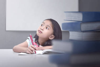 快樂的亞洲小女孩用書本和鋼筆思考