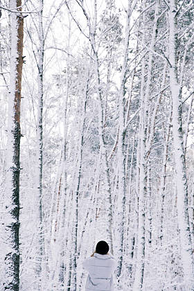 在白雪皑皑的森林里行走的女孩的后视图